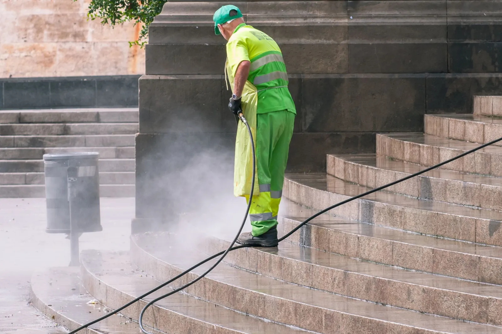 Worker in a green safety suit pressure washing outdoor stone steps